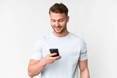 İzole edilmiş beyaz arka planı olan yakışıklı beyaz bir adam cep telefonuyla mesaj ya da e-posta yolluyor.