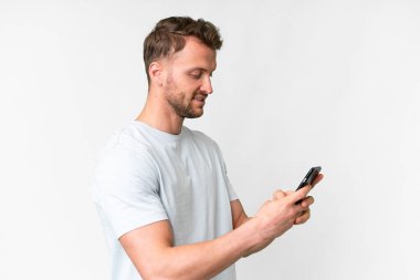 İzole edilmiş beyaz arka planı olan yakışıklı beyaz bir adam cep telefonuyla mesaj ya da e-posta yolluyor.