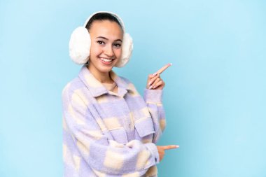 Mavi arka planda izole edilmiş kışlık kuklalar giyen genç bir Arap kadını işaret ediyor ve bir ürün sunuyor.