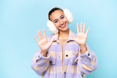 Mavi arka planda izole edilmiş kışlık kuklalar giyen genç bir Arap kadın parmaklarıyla 10 tane sayıyor.