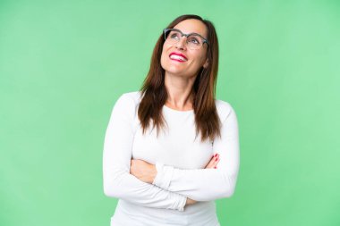 Middle age woman over isolated chroma key background looking up while smiling