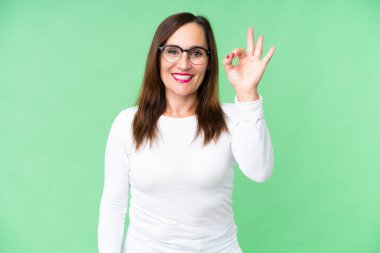 Middle age woman over isolated chroma key background showing ok sign with fingers