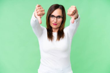 Middle age woman over isolated chroma key background showing thumb down with two hands