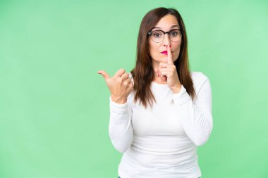 Orta yaşlı kadın izole edilmiş krom anahtar arka planda yan tarafı gösteriyor ve sessizlik jesti yapıyor.