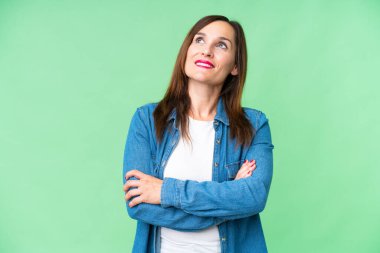Middle age woman over isolated chroma key background looking up while smiling