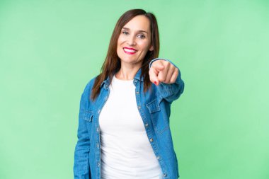 Orta yaşlı bir kadın izole edilmiş krom anahtar arka planda kendine güvenen bir ifadeyle seni işaret ediyor.