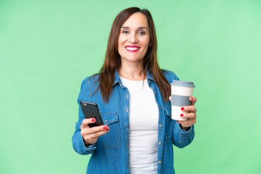 Orta yaşlı bir kadın izole edilmiş krom anahtar geçmişi var. Elinde kahve ve cep telefonu var.