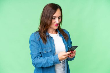 Middle age woman over isolated chroma key background sending a message with the mobile