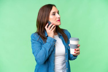 Orta yaşlı bir kadın izole edilmiş krom anahtar geçmişi var. Elinde kahve ve cep telefonu var.