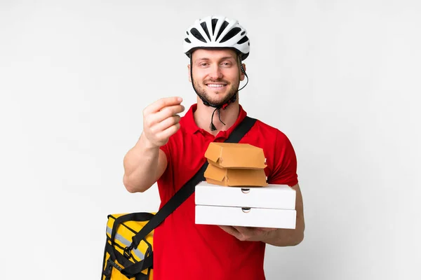 stock image Young delivery man taking a takeaway food over isolated white background making money gesture