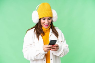 Orta yaşlı kadın izole edilmiş krom anahtar arkaplan üzerine kış maskesi takıyor cep telefonuyla bir mesaj gönderiyor.