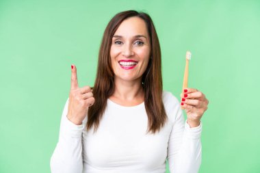 Orta yaşlı bir kadın, izole edilmiş krom arka planda dişlerini fırçalıyor. Harika bir fikir.