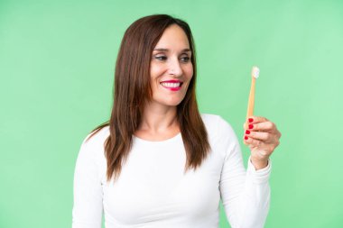 Orta yaşlı bir kadın izole edilmiş krom anahtar arka planda mutlu bir ifadeyle dişlerini fırçalıyor.