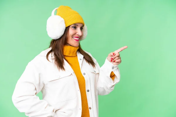中年妇女穿着冬衣 罩在孤立的彩色关键背景上 手指指向侧面 并展示了一种产品 — 图库照片