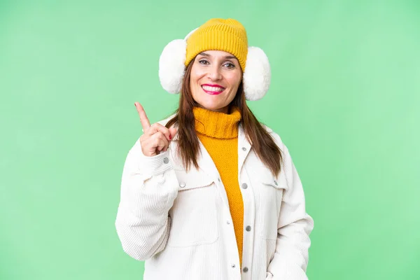 中年妇女披着冬衣 挂在孤立的彩色关键背景上 露出并举起一个手指 这标志着最好的标志 — 图库照片