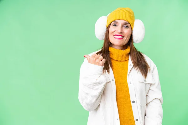 中年妇女披着冬衣 罩在孤立的彩色关键背景上 指着侧面展示自己的产品 — 图库照片