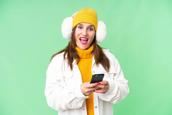 stock image Middle age woman wearing winter muffs over isolated chroma key background surprised and sending a message