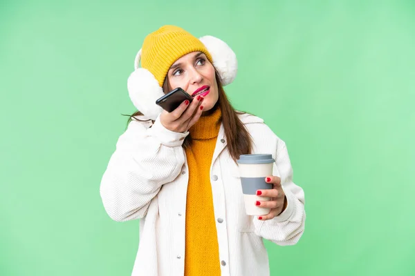 中年妇女披着冬衣 披着孤立的彩色关键背景 拿着咖啡和手机走了 — 图库照片