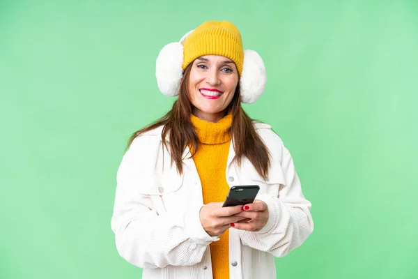 中年妇女披着冬衣 罩在孤立的彩色关键背景上 用手机传递信息 — 图库照片