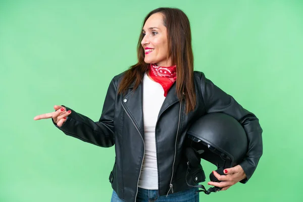 中年高加索女人 头戴摩托车头盔 头戴独立的彩色关键背景 手指指向侧面 展示产品 — 图库照片