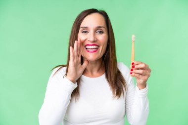 Orta yaşlı bir kadın dişlerini fırçalarken izole edilmiş krom anahtar arka planda ağzı açık bağırıyor.