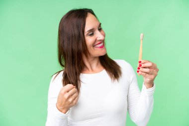 Middle age woman brushing teeth over isolated chroma key background celebrating a victory