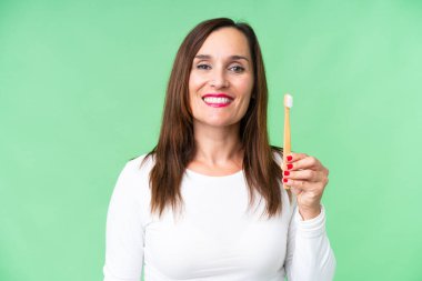 Orta yaşlı bir kadın izole edilmiş krom arka planda dişlerini fırçalıyor. Çok gülümsüyor.