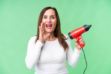 Orta yaşlı bir kadın, elinde saç kurutma makinesini izole edilmiş krom anahtar arka planda tutarak ağzı açık bağırıyor.