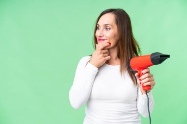 Orta yaşlı bir kadın elinde saç kurutma makinesini izole edilmiş krom anahtar arka planda tutarak bir fikir üretiyor ve bir tarafa bakıyor.