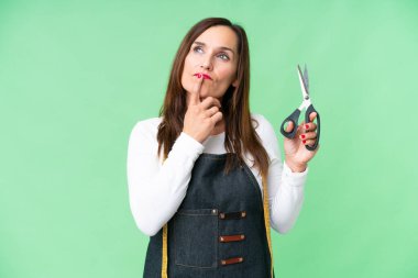 Seamstress woman over isolated chroma key background having doubts while looking up