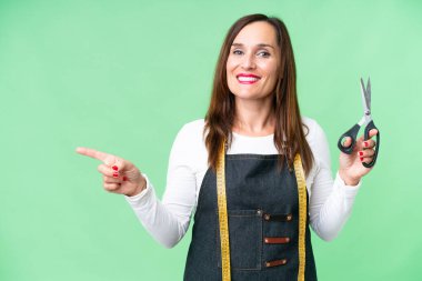 Seamstress woman over isolated chroma key background pointing finger to the side