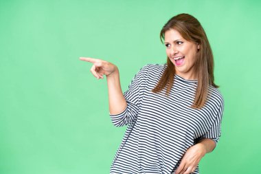 Middle age woman over isolated background pointing finger to the side and presenting a product