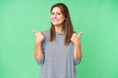 Orta yaşlı bir kadın soyutlanmış bir geçmişle baş parmak işareti ve gülümseme ile