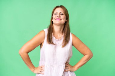 Orta yaşlı kadın soyutlanmış arka planda kolları kalçasında poz veriyor ve gülümsüyor