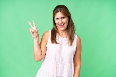 Orta yaşlı bir kadın, izole edilmiş arka planda gülümsüyor ve zafer işareti gösteriyor.