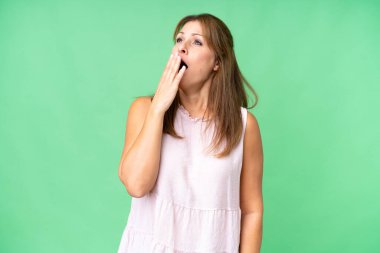 Middle age woman over isolated background yawning and covering wide open mouth with hand