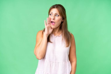 Orta yaşlı bir kadın, izole edilmiş arka planda, yan tarafa bakarken sürpriz bir hareketle bir şeyler fısıldıyor.