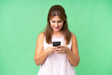 İzole edilmiş arka planda orta yaşlı bir kadın cep telefonuyla mesaj gönderiyor.