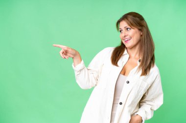 Middle age woman over isolated background pointing finger to the side and presenting a product