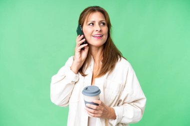 Orta yaşlı bir kadın izole edilmiş arka planda kahve ve bir cep telefonu tutuyor.