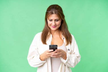 İzole edilmiş arka planda orta yaşlı bir kadın cep telefonuyla mesaj gönderiyor.