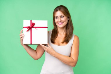 Middle age caucasian woman holding a gift over isolated background with happy expression