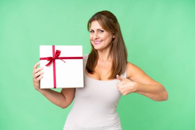 Orta yaşlı beyaz bir kadın, iyi bir şey olduğu için izole edilmiş bir geçmişi olan bir hediye tutuyor.