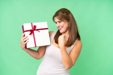 Orta yaşlı, beyaz bir kadın, izole bir arkaplanda bir hediye tutuyor ve zaferi kutluyor.