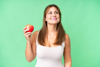 Arkaplanda elma olan orta yaşlı bir kadın gülümserken yukarı bakıyor.