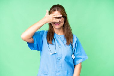 Orta yaşlı bir hemşire, izole edilmiş bir geçmişi var. Gözlerini elleriyle kapatıyor ve gülümsüyor.