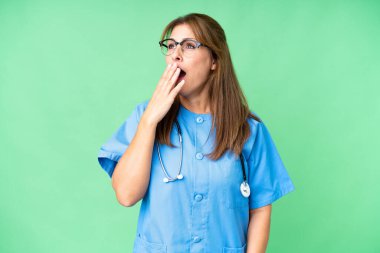 Orta yaşlı hemşire kadın izole edilmiş arka planda esniyor ve ağzını eliyle açık tutuyor.