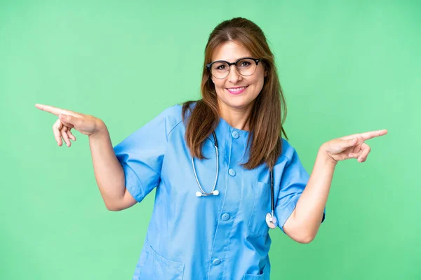 Pielęgniarka Średnim Wieku Ponad Odosobnionym Tle Wskazując Palcem Boki Szczęśliwy — Zdjęcie stockowe