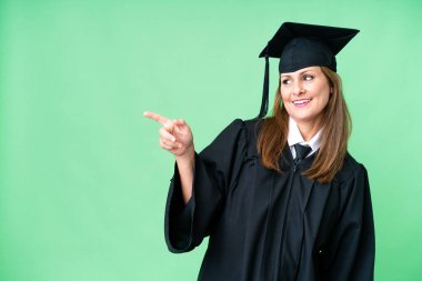 Middle age university graduate woman over isolated background pointing finger to the side and presenting a product