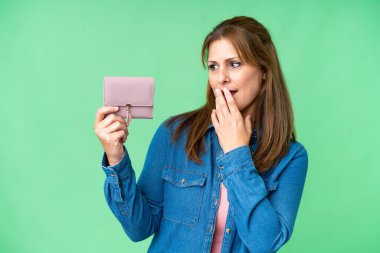 Orta yaşlı, beyaz bir kadın cüzdanı soyutlanmış, şaşırmış ve şok olmuş bir yüz ifadesiyle elinde tutuyor.